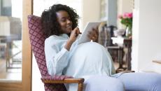 A pregnant person sitting in a chair while looking at a tablet