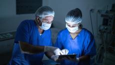 Two healthcare providers consulting a tablet in the operating room