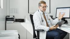 A doctor using a tablet at his desk in a clinic. 