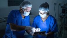 Two people wearing scrubs and masks in a procedure room look at a tablet. 