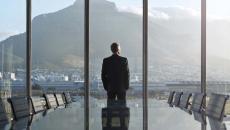 Person standing by a large window with their back turned looking at a large mountain