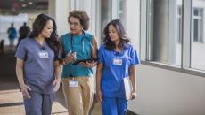 Three people walking down a hall, two healthcare providers in scrubs and one person in civilian clothing