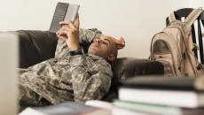 A soldier using a tablet while lying on a sofa. 