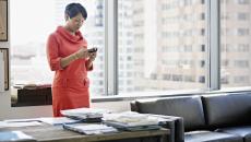 A woman standing at her desk using a smartphone.